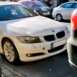White BMW sedan with front-end damage parked on a busy city street.