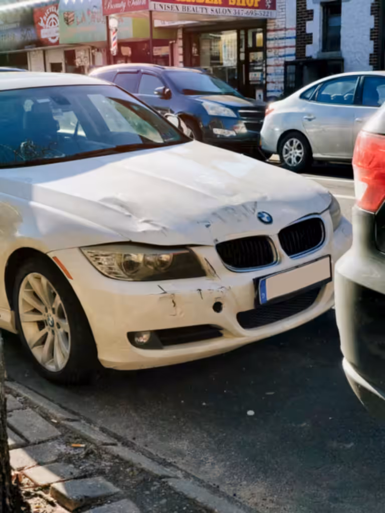 White BMW sedan with front-end damage parked on a busy city street.